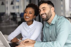 Coworkers laughing together while looking at a laptop in an office