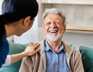 Caregiver resting a hand on an elderly man's shoulder as he laughs