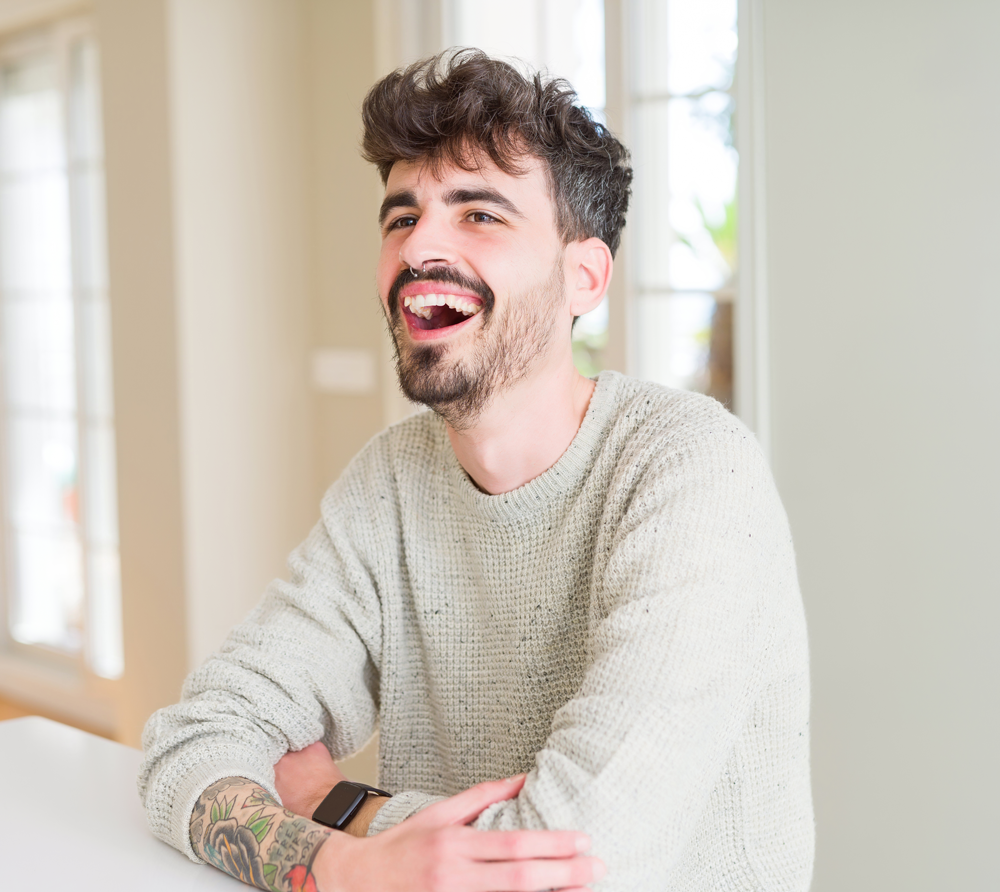 Young man with tattoos laughing indoors near a bright window