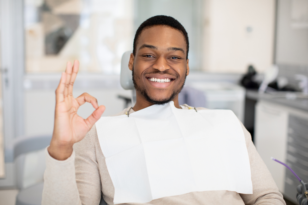 Man in a dental chair smiling and giving an OK hand gesture after treatment