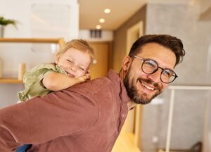 Father carrying his smiling toddler on his back inside their home
