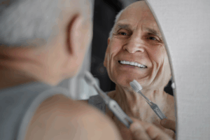 Older man brushing his teeth in front of the bathroom mirror